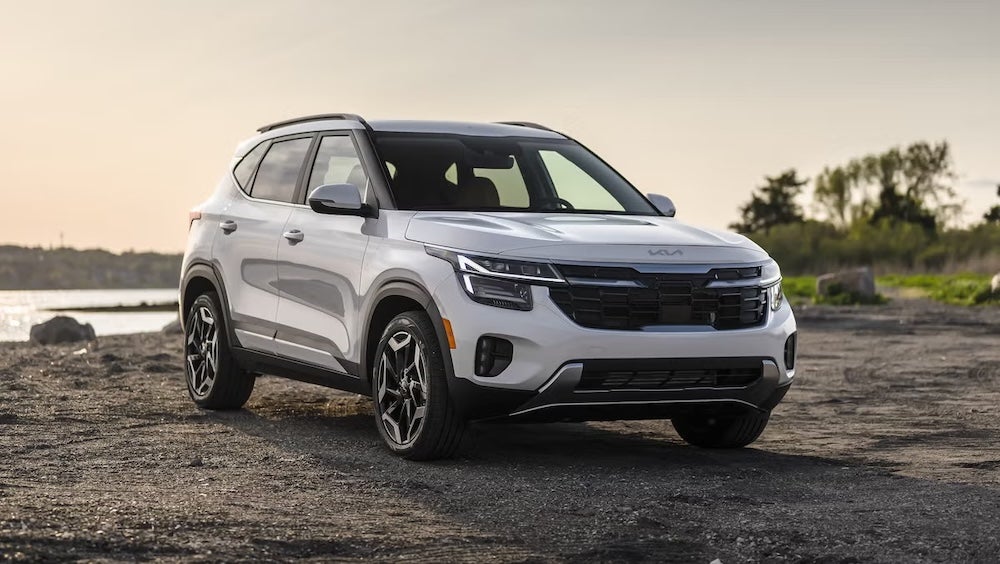 A white 2026 Kia Seltos SUV parked on the beach at sunset