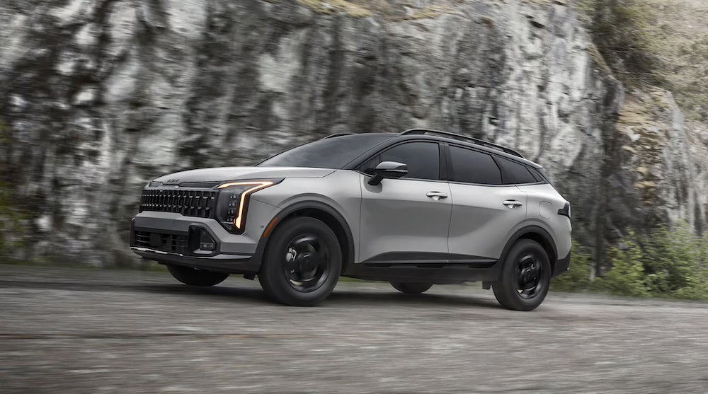 A gray 2027 Kia Sportage SUV driving beside a cliff face
