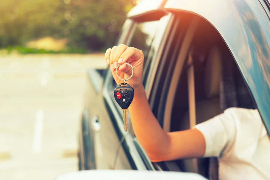 A person holding a set of car keys out the open window of a car